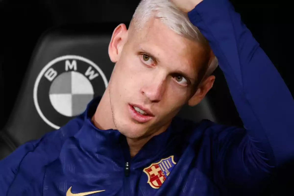 Un jugador de fútbol con cabello rubio platino y chaqueta azul con el escudo del FC Barcelona se toca la cabeza mientras está sentado frente a un logotipo de BMW.