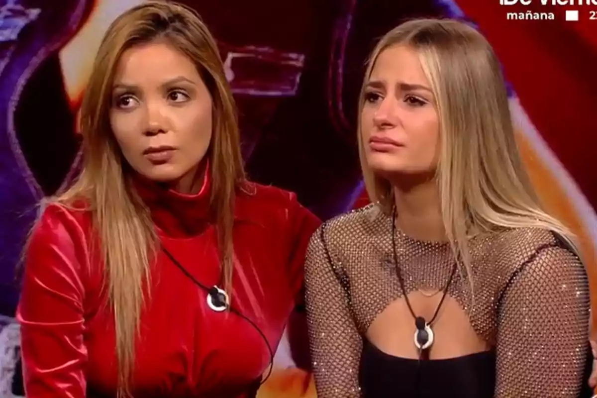 Daniela y Laura Galera sentadas en Gran Hermano, una con un vestido rojo y la otra con un top de malla, ambas con expresiones serias.