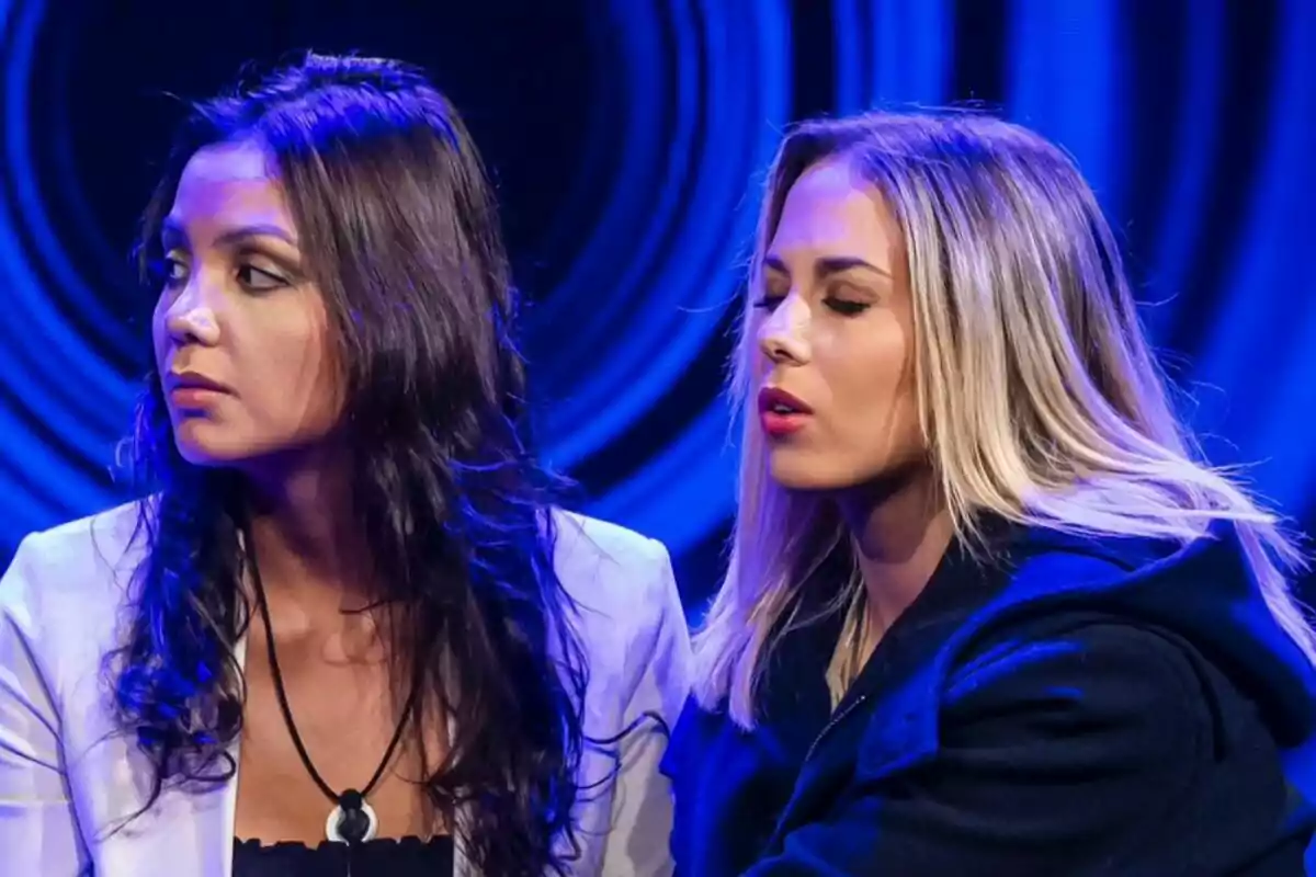 Daniela y Violeta sentadas en un ambiente iluminado con luces azules en Gran Hermano, una de ellas con el cabello oscuro y la otra rubia.