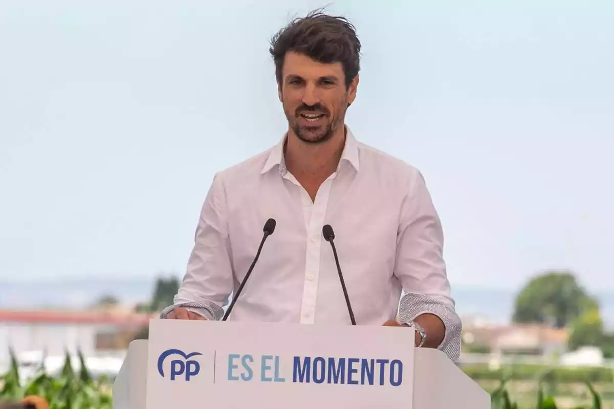 Plano medio de Dante Pérez con camisa blanca hablando desde un atril con el lema 'Es el momento' y el logo del PP