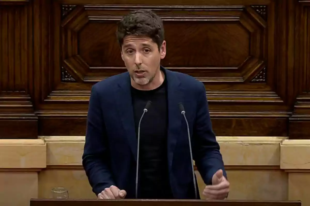 Un hombre hablando en un podio con un fondo de madera decorativa. Un hombre hablando en un podio con un fondo de madera decorativa.
