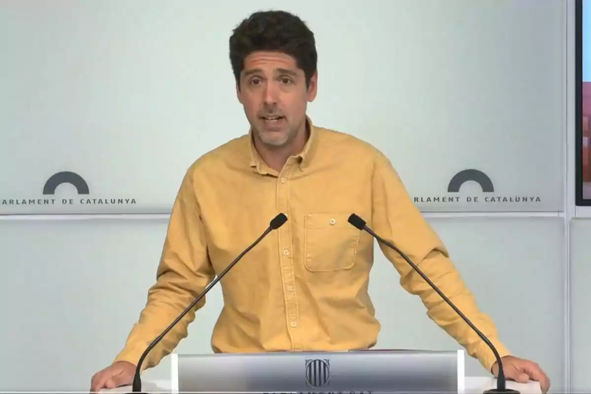 Un hombre con camisa amarilla habla en un podio con el logo del Parlament de Catalunya.