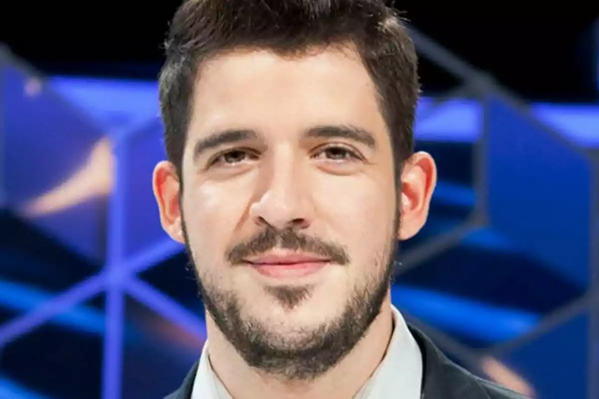 David Leo con barba y cabello oscuro sonríe frente a un fondo azul geométrico en El Cazador.