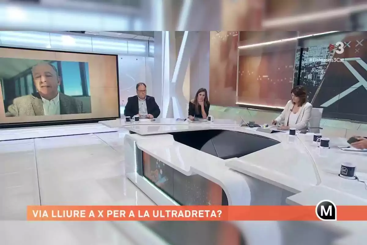 Un grupo de personas participa en un programa de televisión en un estudio moderno, con una pantalla grande mostrando a un hombre y un texto en catalán en la parte inferior.