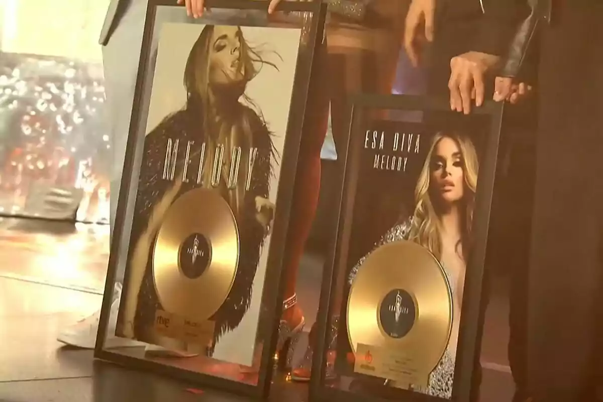 Dos personas sostienen discos de oro enmarcados con imágenes de una artista femenina en la portada. Dos personas sostienen discos de oro enmarcados con imágenes de una artista femenina en la portada.