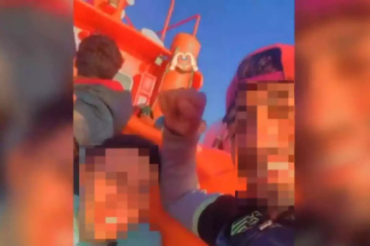 Captura de un vídeo de un inmigrante en un barco con la cara pixelada, mirando a cámara y con gorra, alzando su puño derecho