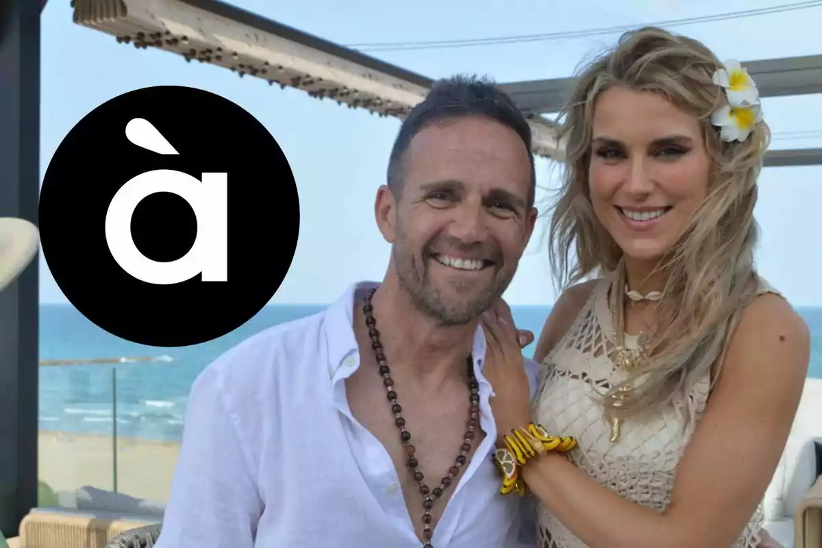 Eduard Forés y Maria Fuster sonriente posa frente al mar en una terraza soleada, junto a un círculo negro con el logo de À Punt