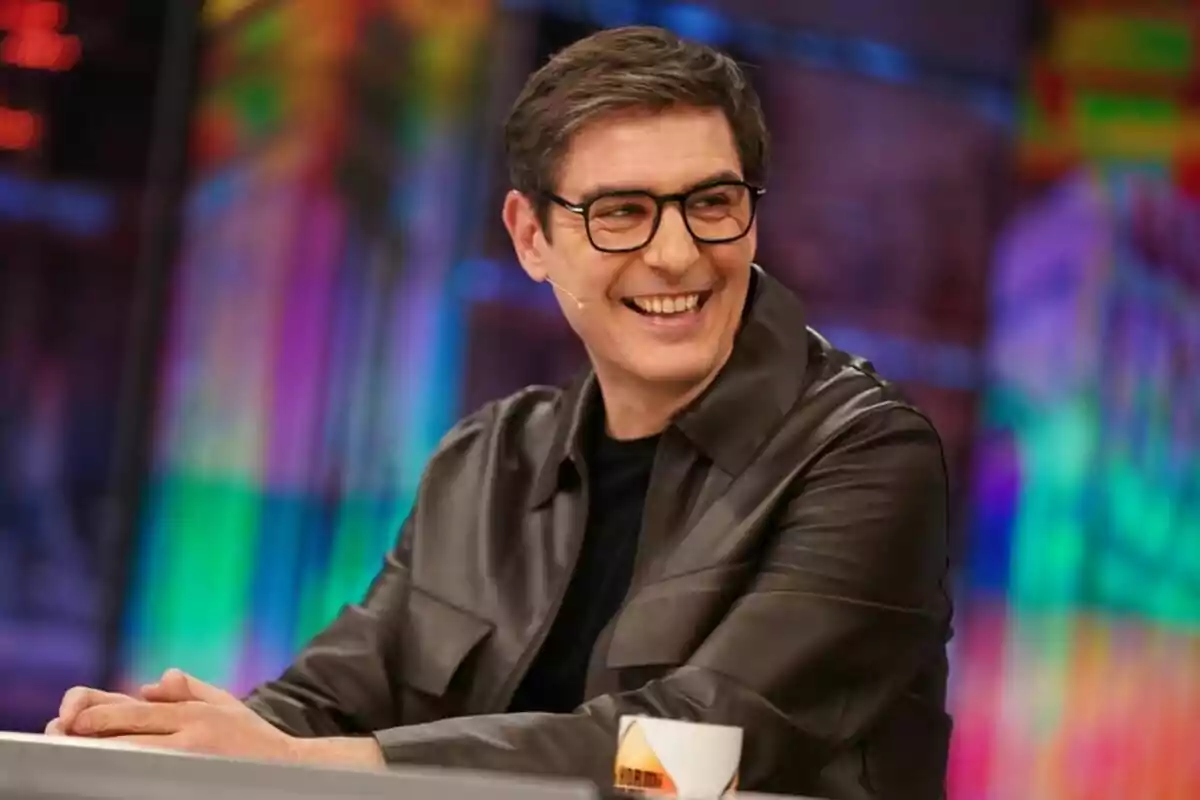 Juanra Bonet con gafas y chaqueta oscura sonríe mientras está sentado en 'El Hormiguero'.