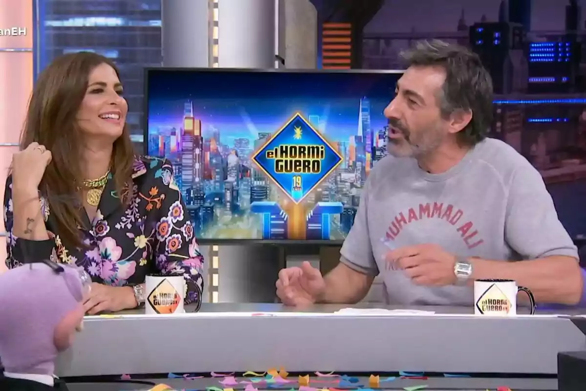 Nuria Roca y Juan del Val conversando y sonriendo en 'El Hormiguero' con un fondo colorido y una mesa llena de confeti. Nuria Roca y Juan del Val conversando y sonriendo en 'El Hormiguero' con un fondo colorido y una mesa llena de confeti.