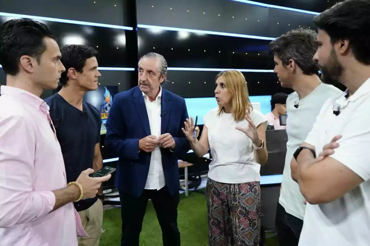 Un grupo de seis personas conversa de pie en un estudio de televisión con fondo oscuro y luces azules, una mujer gesticula mientras los demás la escuchan atentamente en 'El Chiringuito'. Un grupo de seis personas conversa de pie en un estudio de televisión con fondo oscuro y luces azules, una mujer gesticula mientras los demás la escuchan atentamente en 'El Chiringuito'.