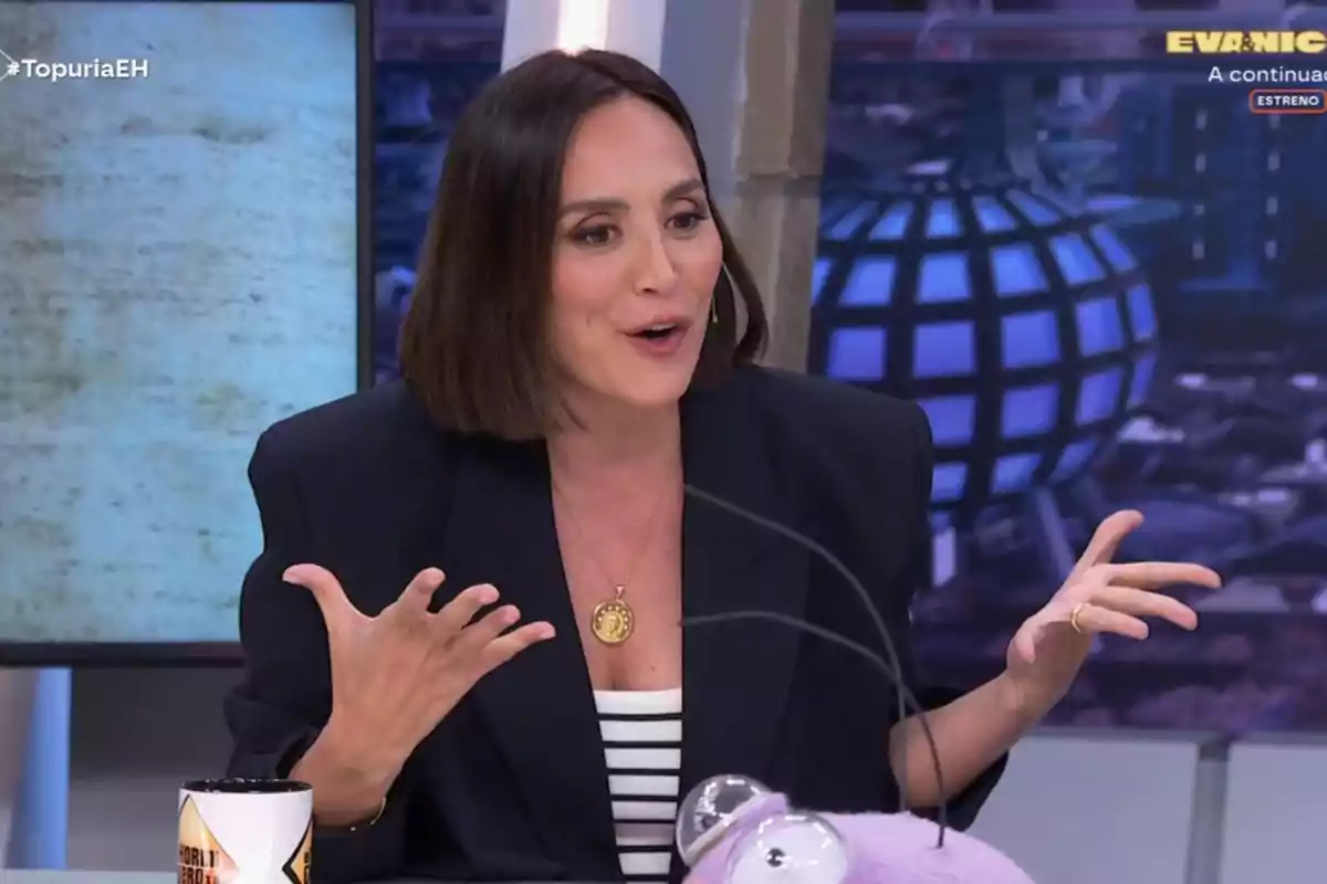 Tamara Falcó está gesticulando mientras habla en un programa de televisión, lleva un collar dorado y una chaqueta oscura, y hay una taza y un objeto morado en la mesa frente a ella. Captura de 'El Hormiguero'