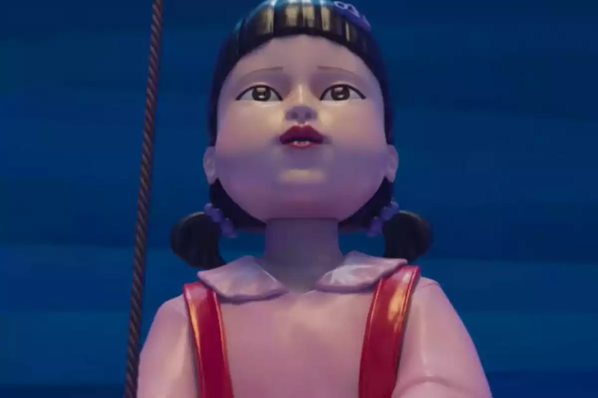 Muñeca gigante con cabello oscuro y vestido rosa observando hacia el frente en un fondo azul de El Juego del Calamar