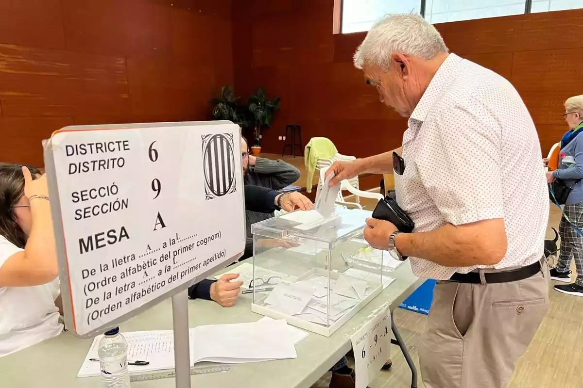 Plano americano de un señor mayor introduciendo su voto en una urna de una mesa electoral en Cataluña