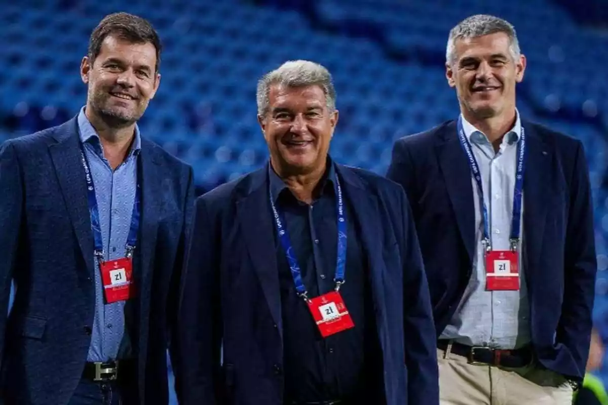 Plano medio de Joan Laporta, Enric Masip y otro directivo del FC Barcelona sonriendo en un estadio con asientos azules de fondo