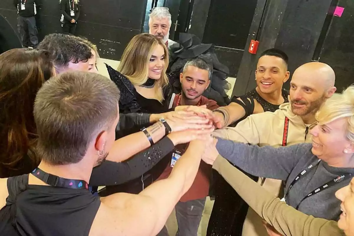 La delegación española de Eurovisión y Melody se reúne en círculo, colocando sus manos juntas en el centro en un gesto de unión y camaradería, mientras sonríen y parecen estar en un ambiente de celebración o preparación para un evento. La delegación española de Eurovisión y Melody se reúne en círculo, colocando sus manos juntas en el centro en un gesto de unión y camaradería, mientras sonríen y parecen estar en un ambiente de celebración o preparación para un evento.