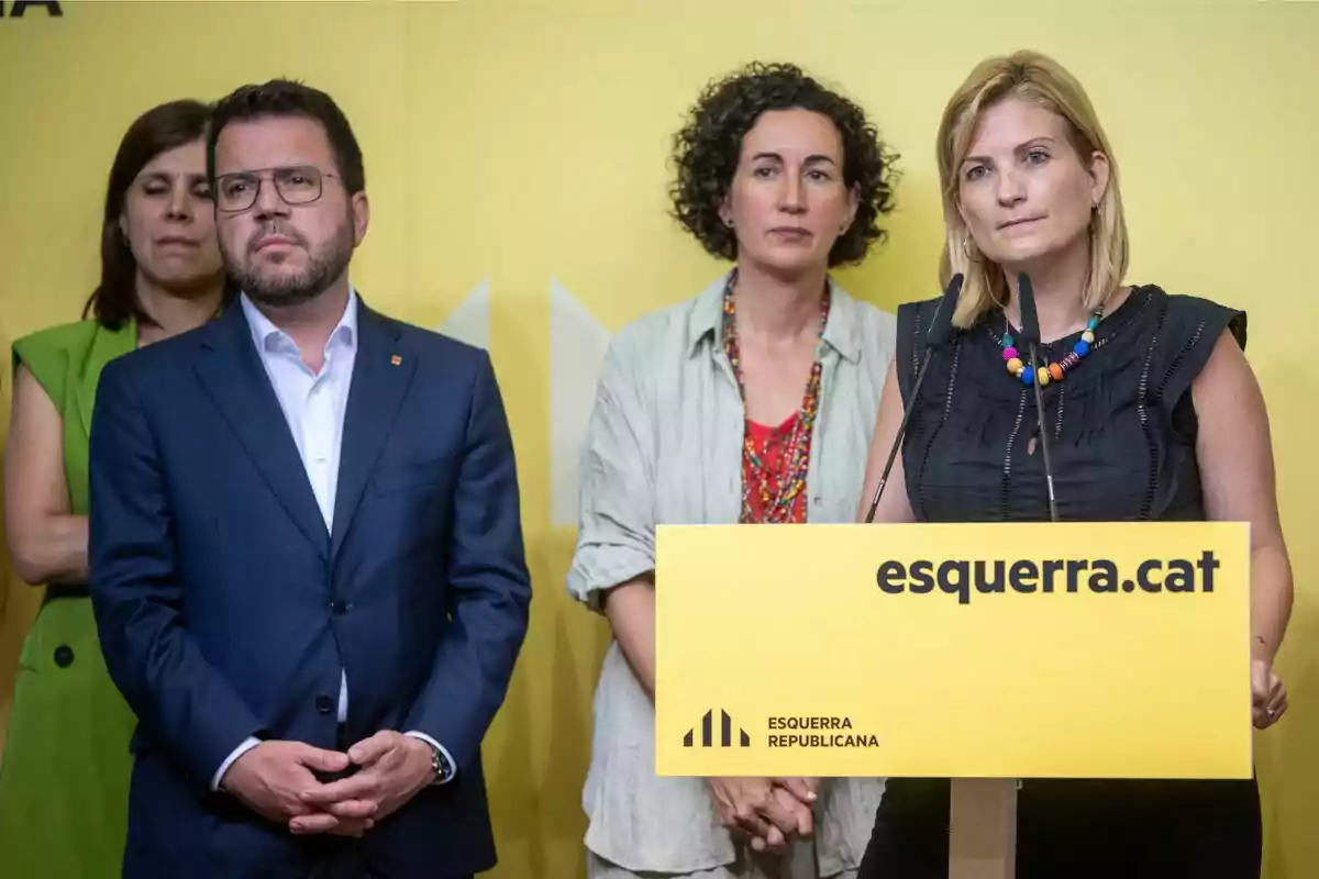 Personas en una conferencia de prensa de Esquerra Republicana con un fondo amarillo y un podio con el logo del partido.