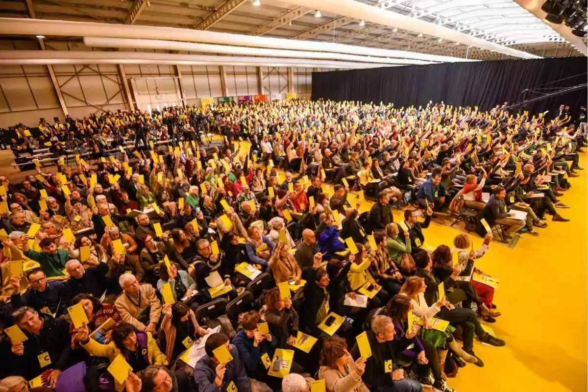 Una multitud de personas sentadas en un auditorio levantando tarjetas amarillas.