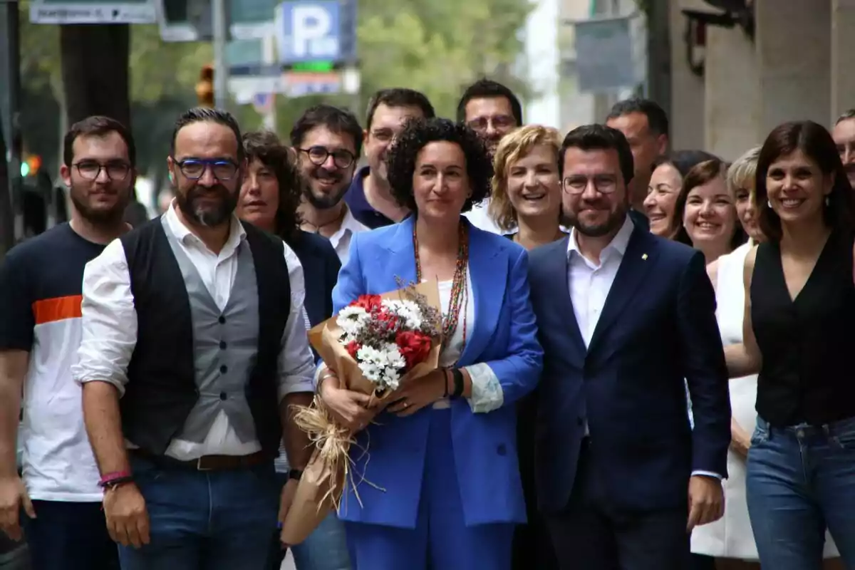 Un grupo de dirigentes de ERC sonrientes posando en una calle, con Marta Rovira en el centro sosteniendo un ramo de flores.