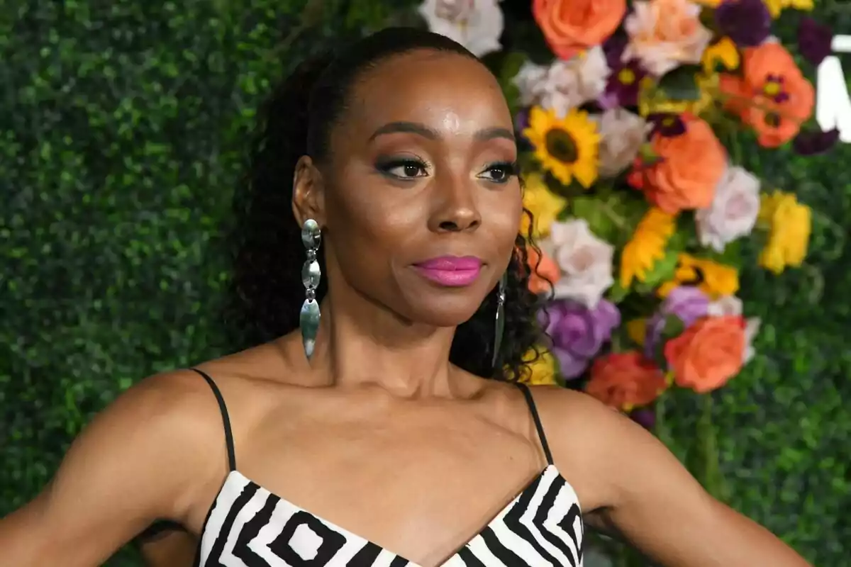 Fotografía de Erica Ash con vestido de rayas y aretes largos posando frente a un fondo de flores y vegetación.