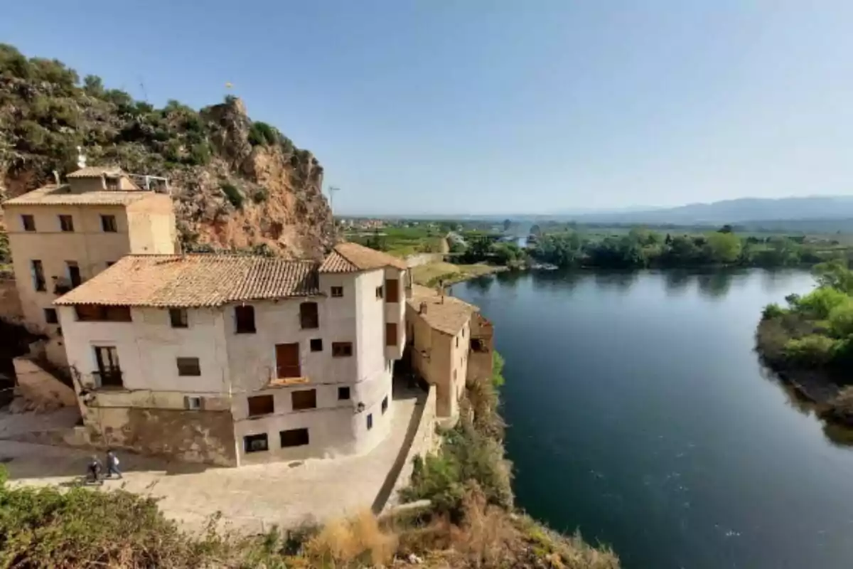 Casas antiguas junto a un río con un paisaje montañoso y vegetación alrededor. Casas antiguas junto a un río con un paisaje montañoso y vegetación alrededor.