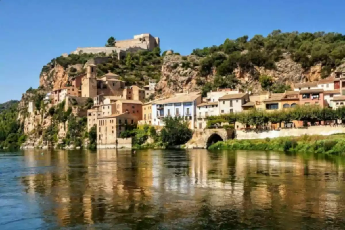 Un pintoresco pueblo con casas coloridas y una fortaleza en lo alto de una colina junto a un río.