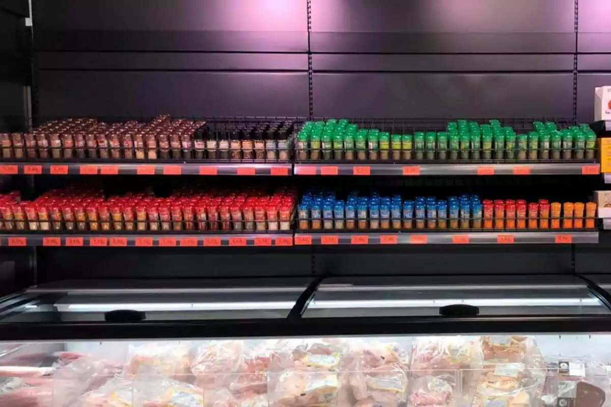 Estantes de supermercado con frascos de especias de diferentes colores y precios, y una vitrina refrigerada con productos cárnicos en la parte inferior. Estantes de supermercado con frascos de especias de diferentes colores y precios, y una vitrina refrigerada con productos cárnicos en la parte inferior.