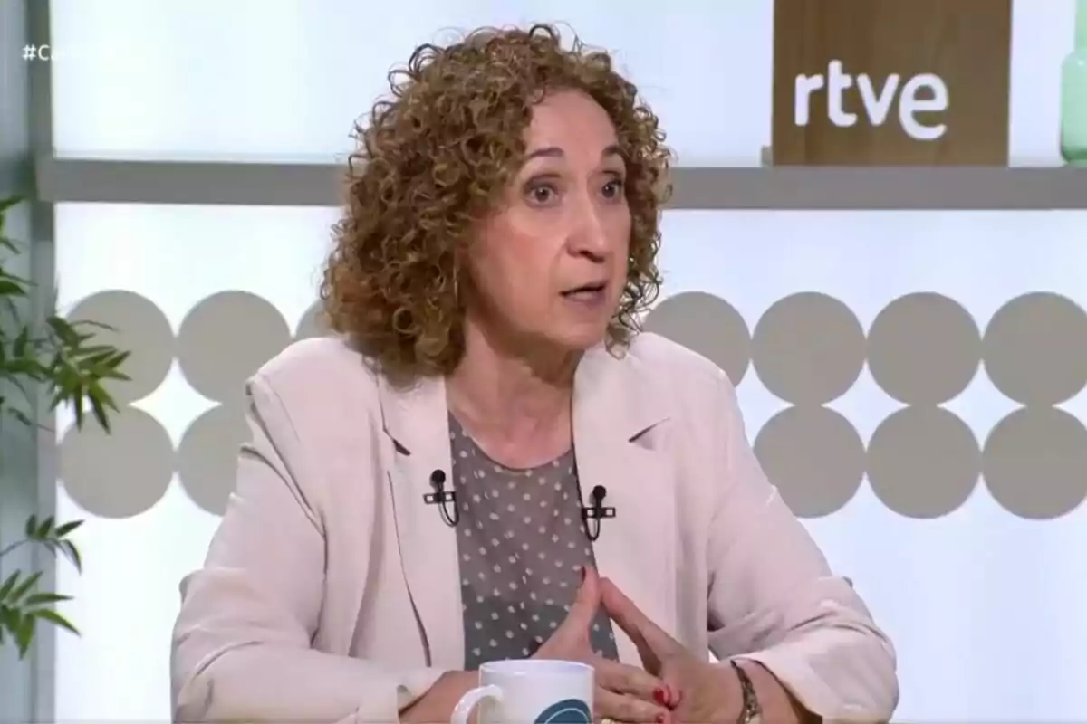 Mujer de cabello rizado y rubio hablando en un programa de televisión con el logo de rtve al fondo