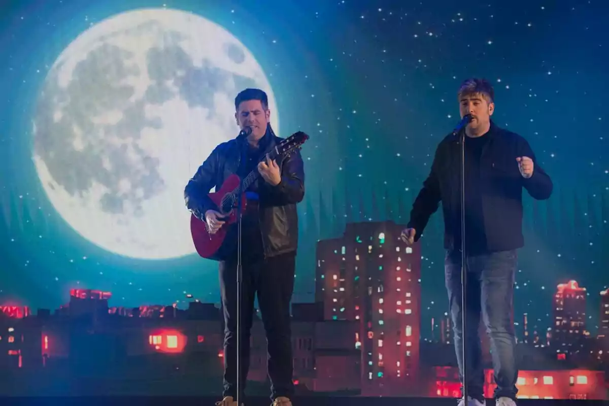 Estopa en un escenario con una guitarra y un micrófono, con un fondo de luna llena y edificios iluminados en el especial de Nochebuena de RTVE.