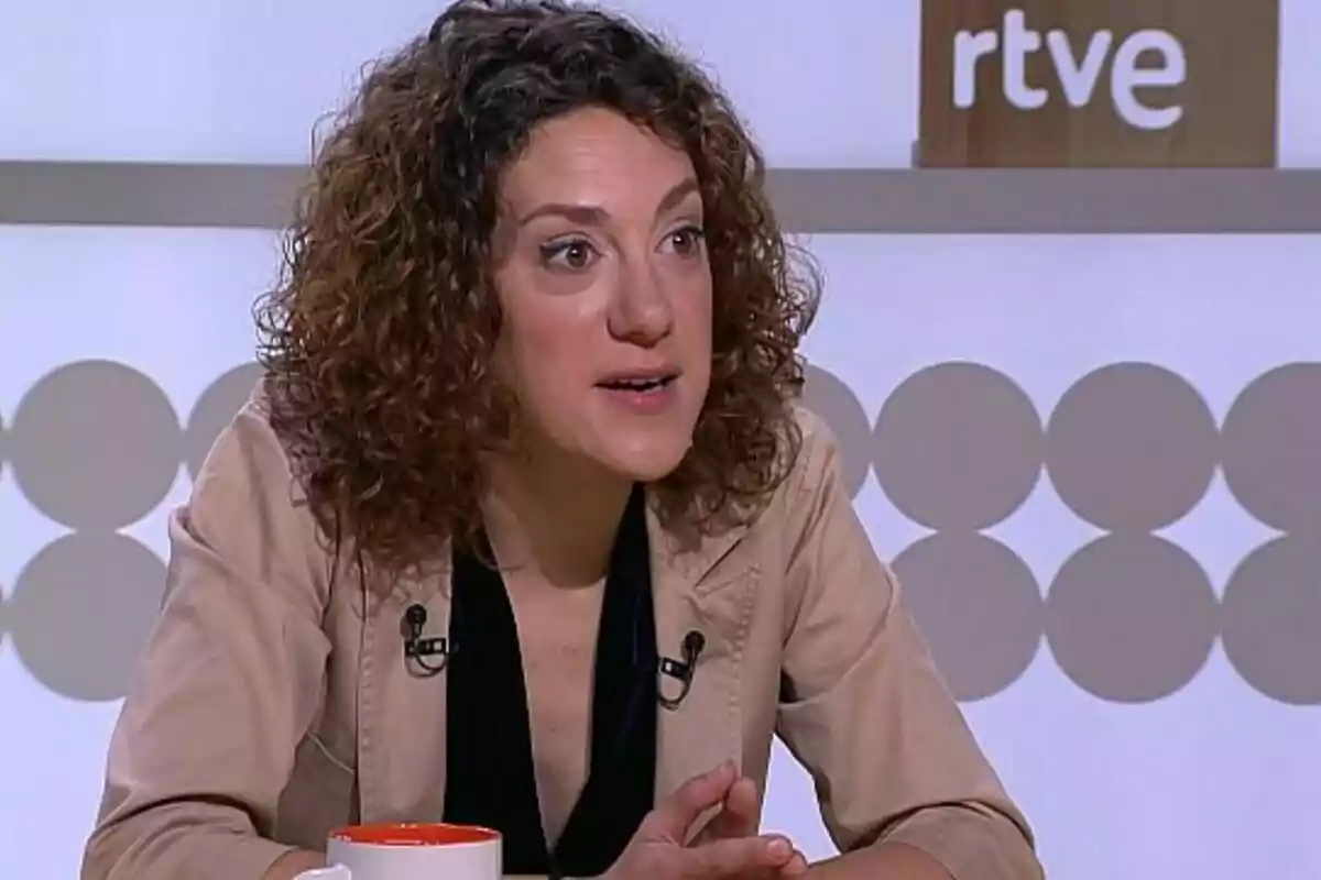 Mujer de cabello rizado hablando en un programa de televisión con el logo de RTVE al fondo.