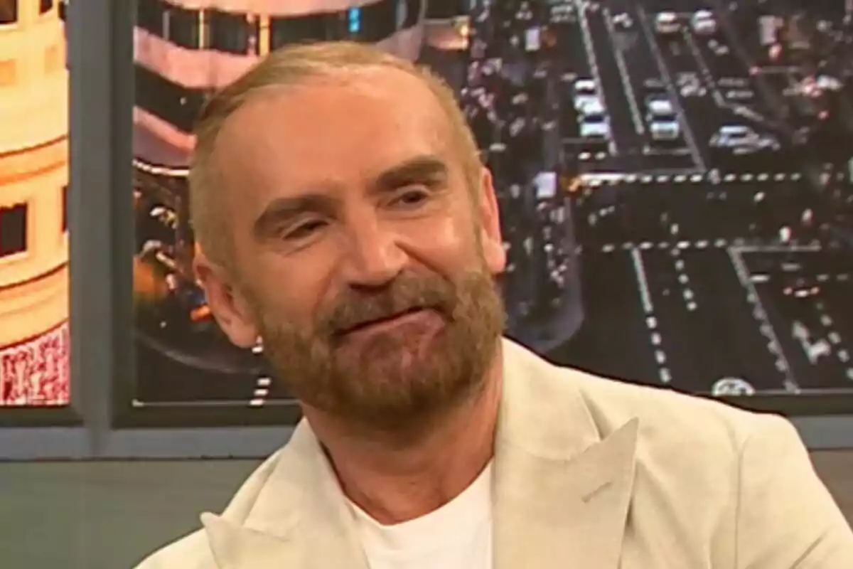 Euprepio Pádula con barba y cabello corto viste un traje claro mientras sonríe en un estudio de televisión con una imagen de una ciudad de fondo en D Corazón. Euprepio Pádula con barba y cabello corto viste un traje claro mientras sonríe en un estudio de televisión con una imagen de una ciudad de fondo en D Corazón.