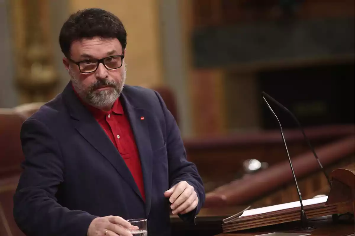 Joan Josep Nuet está de pie en el atril del Congreso de los Diputados sosteniendo un vaso de agua.