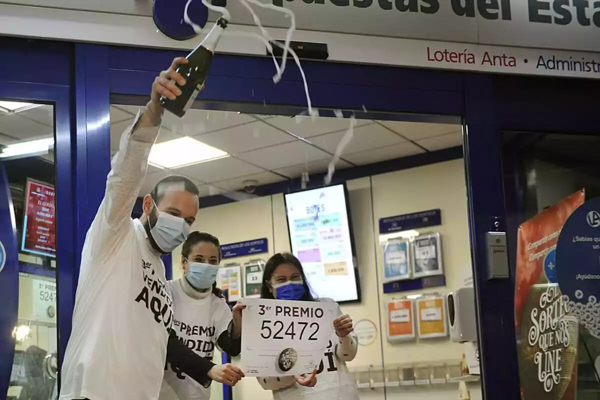 Tres personas celebrando con una botella de cava que les ha tocado el tercer premio de la Lotería