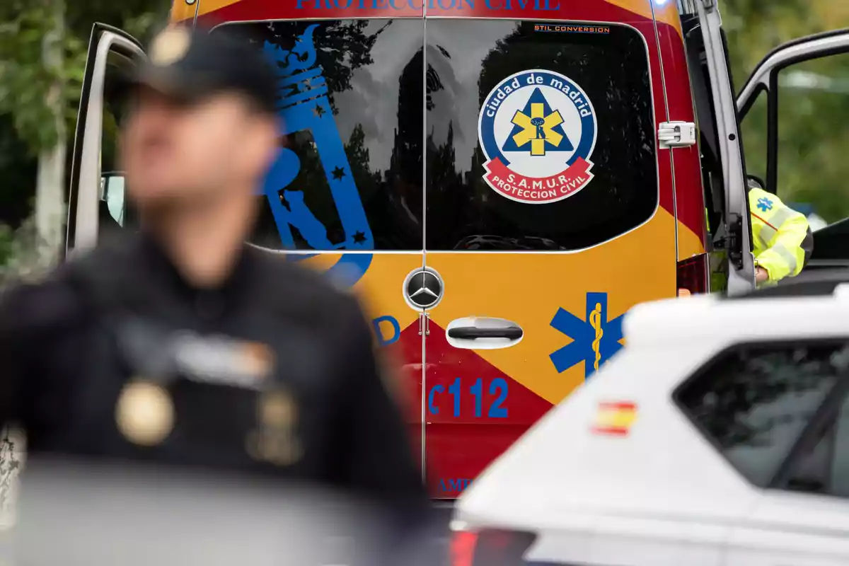 Un vehículo de emergencia del SAMUR de Madrid con un agente de policía desenfocado en primer plano. Un vehículo de emergencia del SAMUR de Madrid con un agente de policía desenfocado en primer plano.