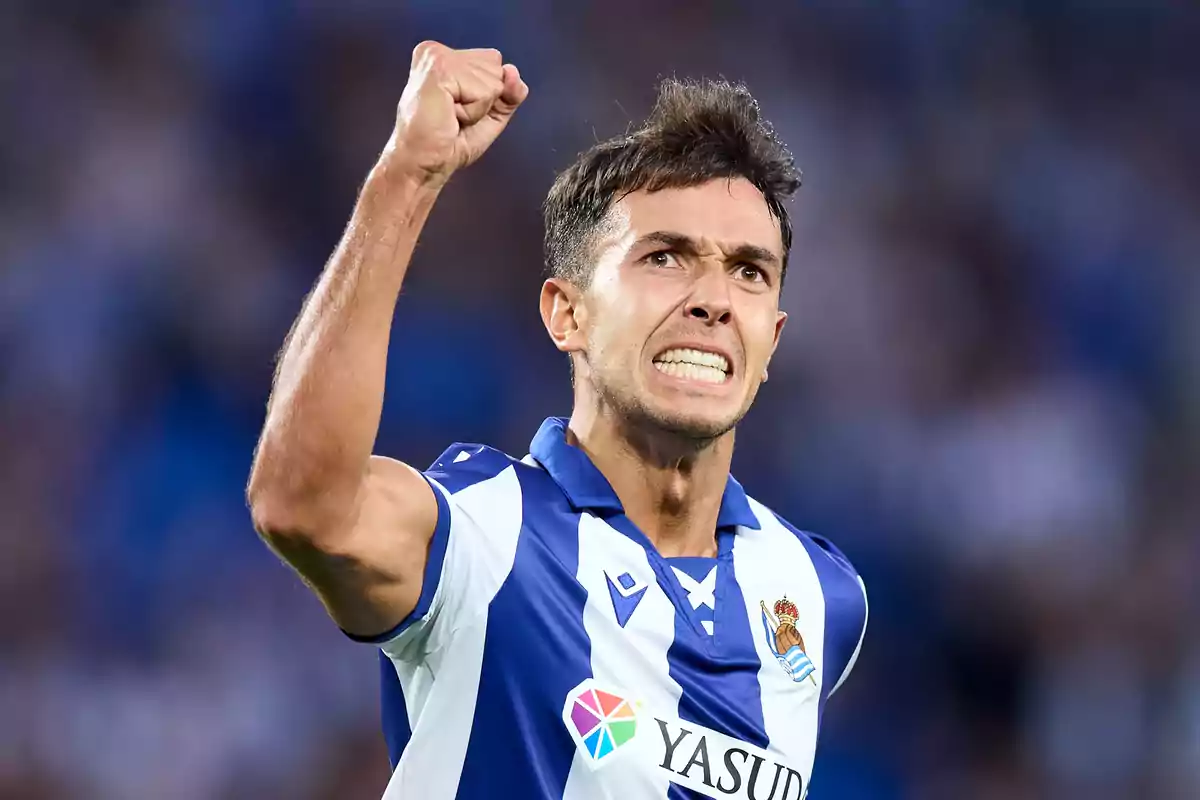 Jugador de fútbol celebrando con el puño en alto mientras viste el uniforme de la Real Sociedad.