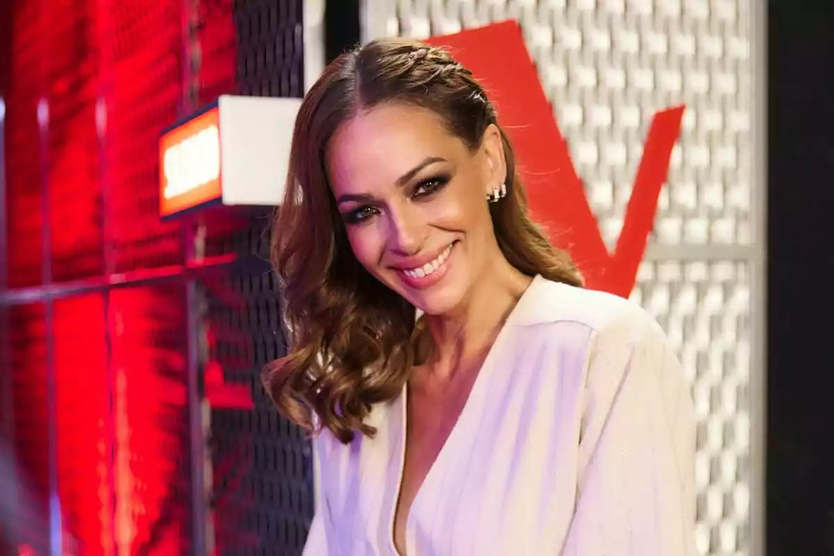 Eva González sonriendo con un fondo rojo y negro en un ambiente iluminado en La Voz Kids. Eva González sonriendo con un fondo rojo y negro en un ambiente iluminado en La Voz Kids.