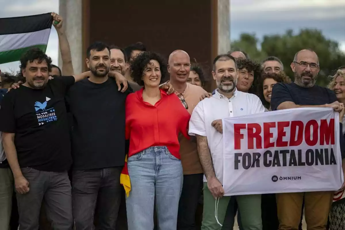 Un grupo de personas sonrientes posando juntas, algunas de ellas sosteniendo una pancarta que dice "FREEDOM FOR CATALONIA" y una bandera en el fondo.