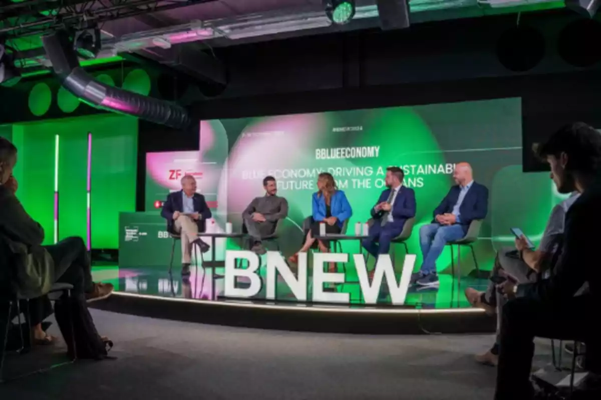 Un panel de discusión sobre economía azul en un escenario con el logo de BNEW y un fondo verde.