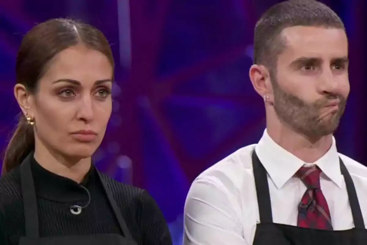 Hiba Abouk y Pelayo Díaz con delantales negros en MasterChef Celebrity con expresiones serias.