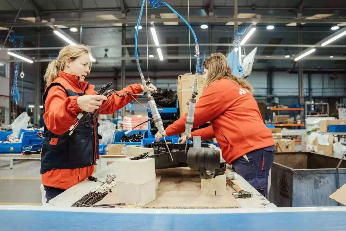 Imagen de dos trabajadoras, una delante de la otra, trabajando y manipulando varias piezas