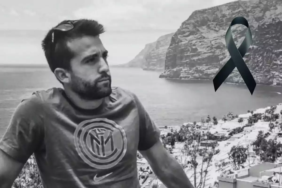 Un hombre con camiseta de un equipo de fútbol y gafas de sol en la cabeza mira hacia el horizonte en un paisaje costero con acantilados y un lazo negro superpuesto en la imagen.