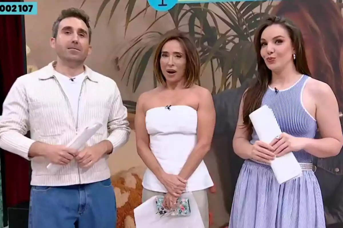 Tres presentadores de televisión, Aitor Albizua, María Patiño e Inés Hernand, posan juntos en un set decorado de La Familia de la Tele con plantas y un fondo beige, cada uno sostiene papeles en las manos y visten ropa casual y elegante