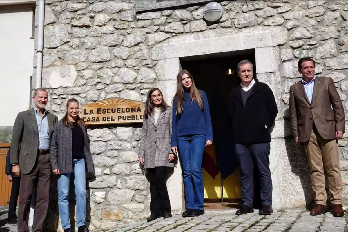 Familia real, junto a autoridades, posando frente a un edificio de piedra con un cartel que dice 