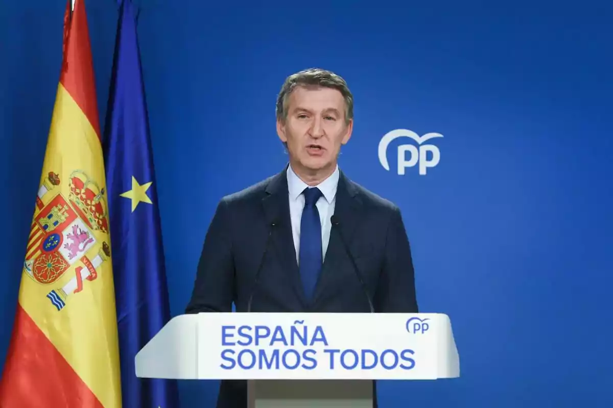 Un hombre en un podio con las banderas de España y la Unión Europea de fondo y el logotipo del PP.