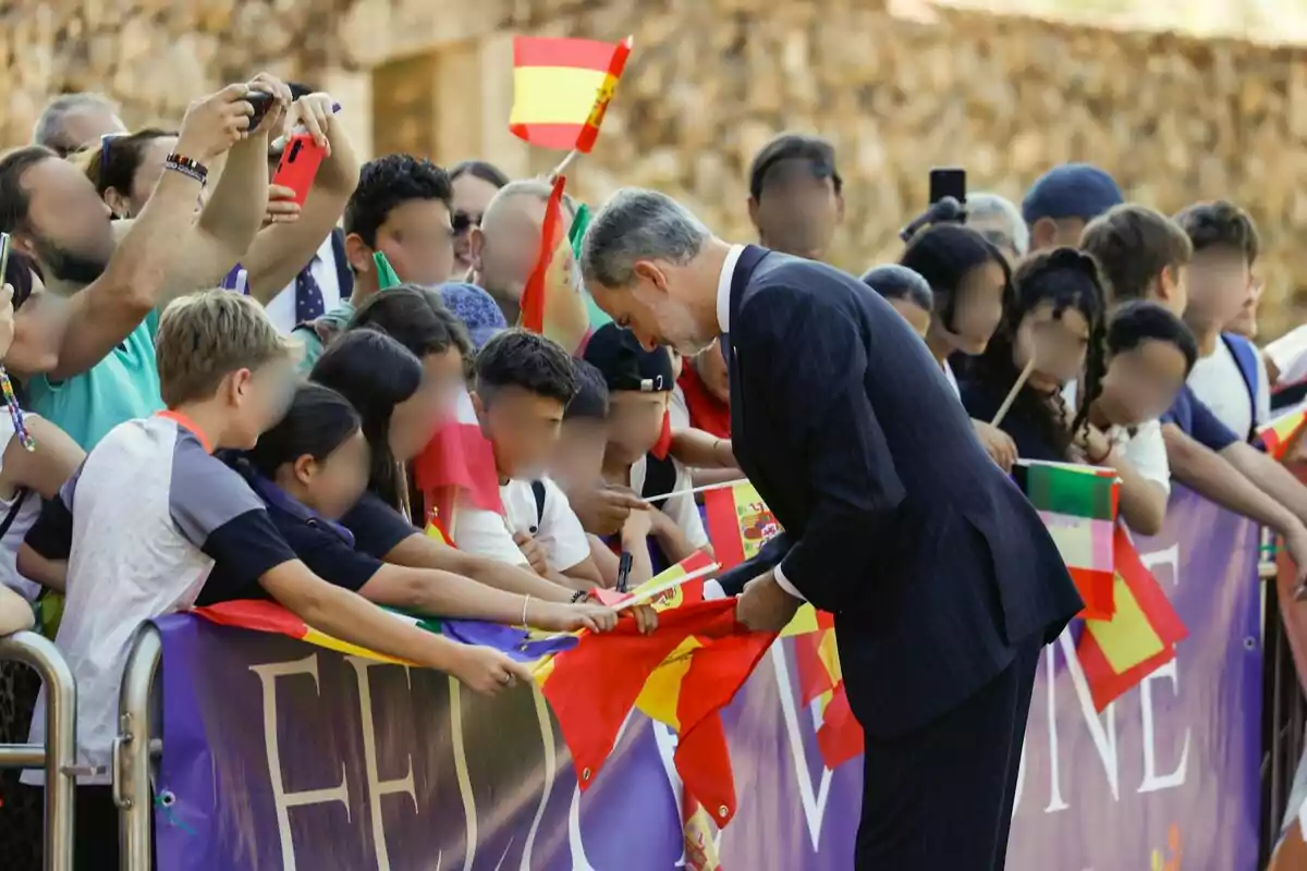 Felipe VI en traje negro agachado firmando autógrafos a unos niños