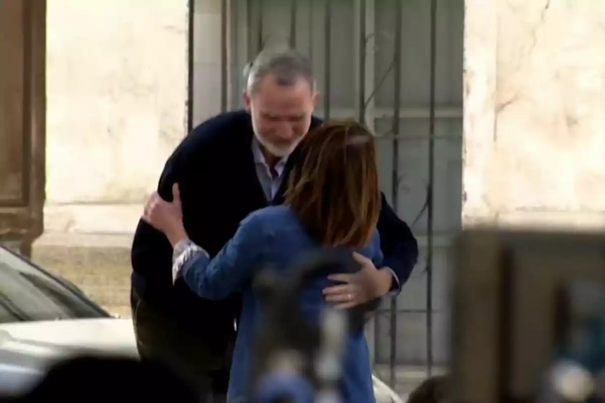 Felipe VI y una mujer se abrazan en una calle frente a un edificio.