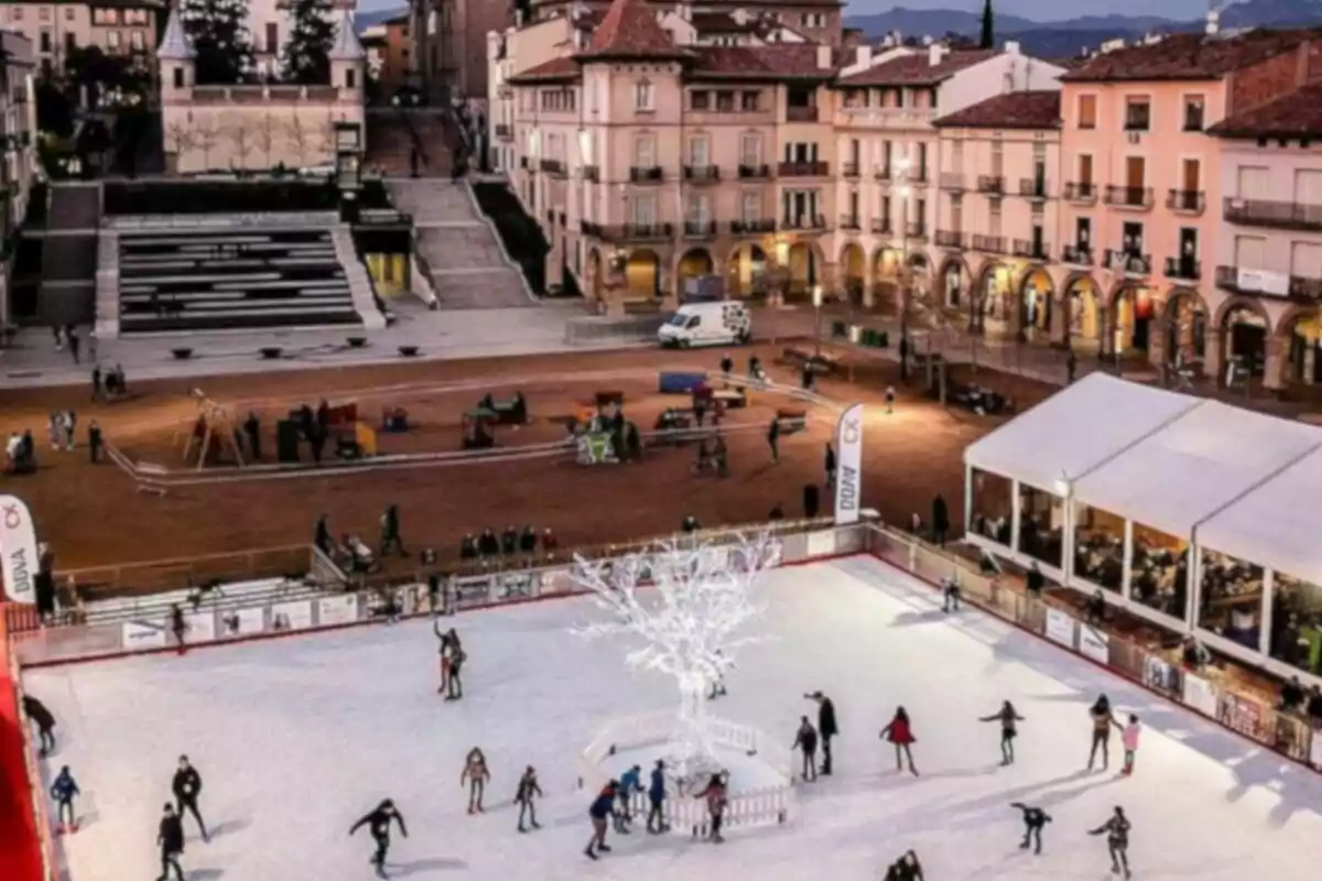 Personas patinando sobre hielo en una pista al aire libre rodeada de edificios históricos y una plaza iluminada.