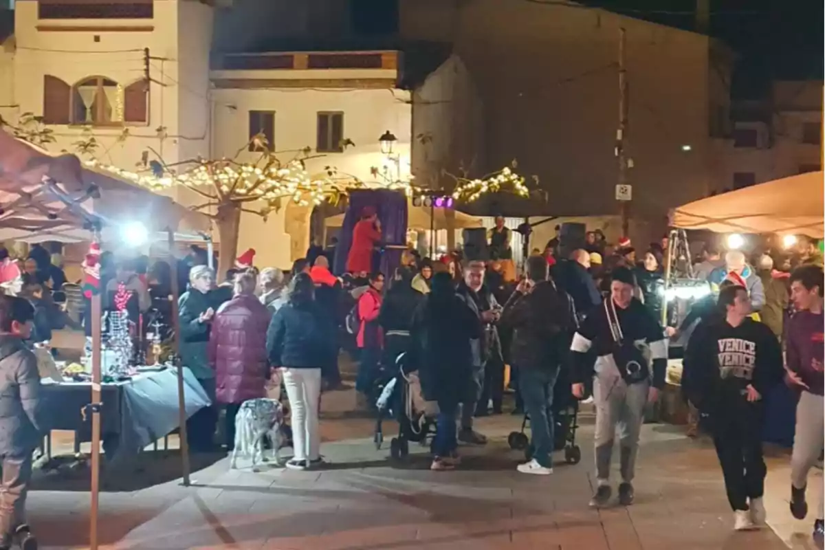 Una plaza iluminada por luces navideñas con personas disfrutando de un mercado nocturno al aire libre. Una plaza iluminada por luces navideñas con personas disfrutando de un mercado nocturno al aire libre.