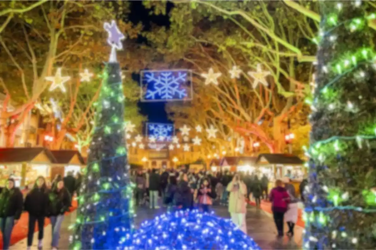 Mercado navideño iluminado con luces de colores y decoraciones festivas, con personas paseando entre los puestos.