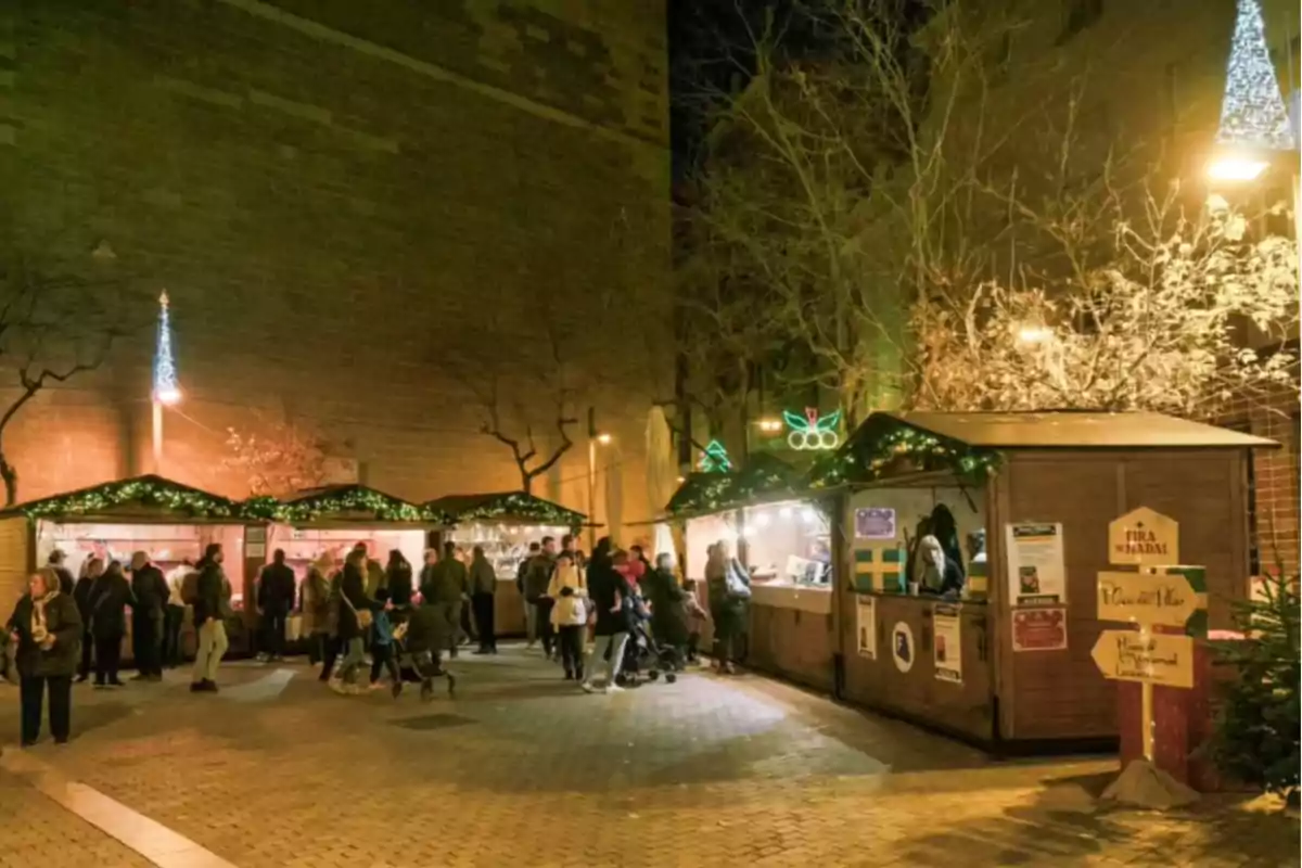 Mercado navideño al aire libre con casetas iluminadas y personas paseando por la noche.