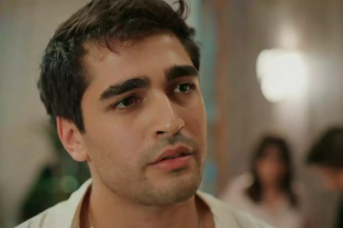 Ferit de cabello oscuro y expresión seria en un ambiente interior desenfocado en Una nueva vida Ferit de cabello oscuro y expresión seria en un ambiente interior desenfocado en Una nueva vida
